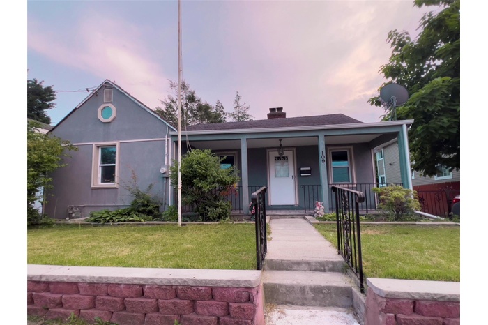 Bungalow featuring a chimney, a porch, a yard, and stucco siding