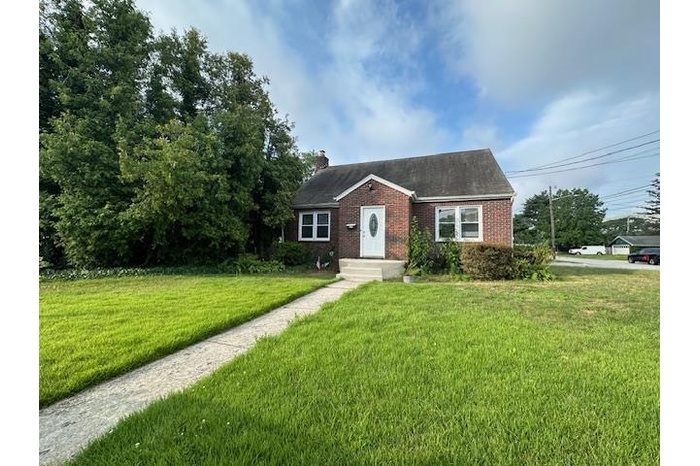 View of front facade featuring a front lawn, a chimney, and brick siding