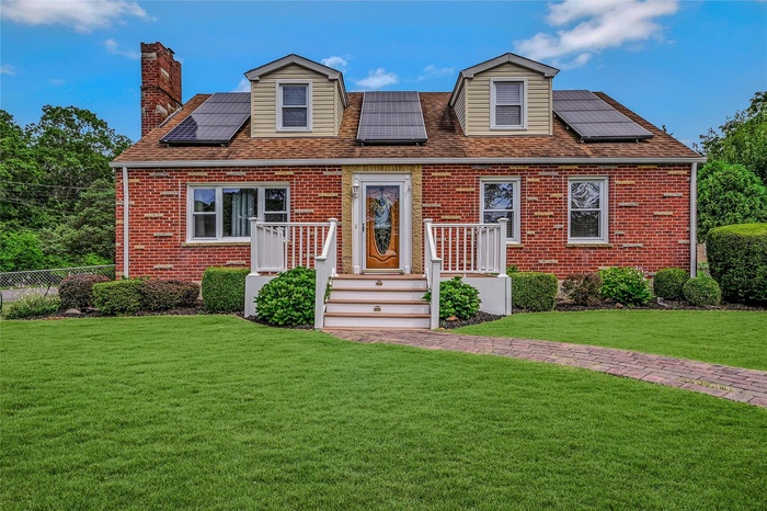 Cape cod home featuring roof mounted solar panels, brick siding, and a chimney