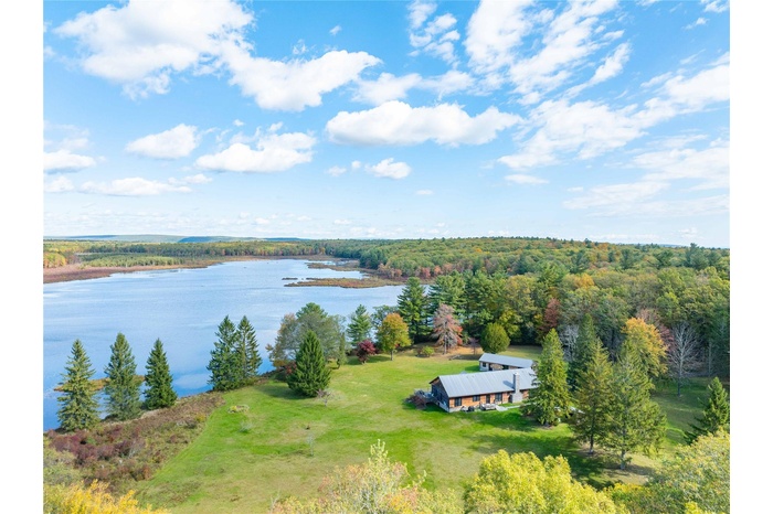 Aerial view of property and surrounding area with a nearby body of water and a heavily wooded area