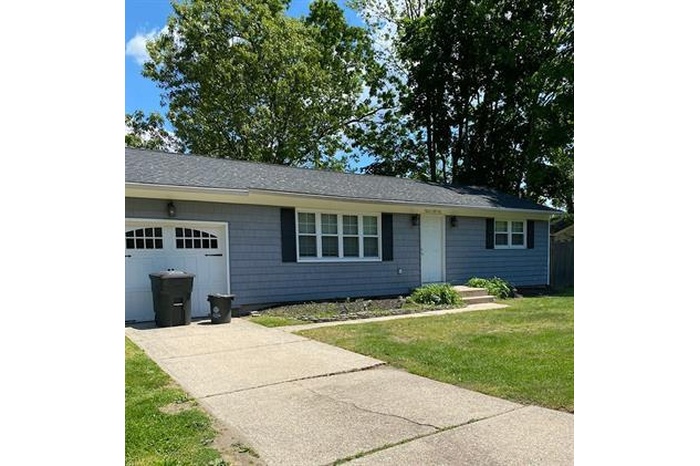 Single story home featuring a garage, driveway, a front yard, and a shingled roof