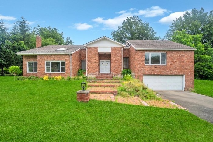 Ranch-style house featuring a chimney, brick siding, asphalt driveway, and a front yard