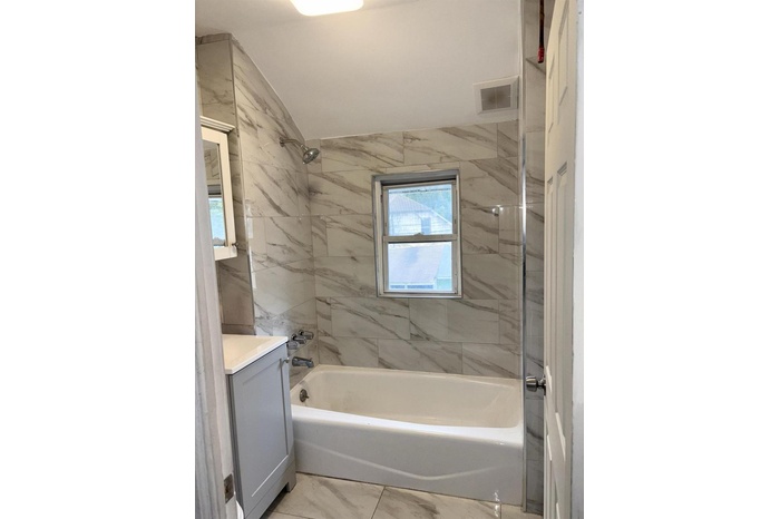 Bathroom with washtub / shower combination, vanity, and marble look tile flooring