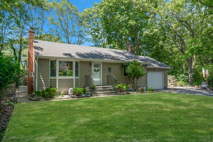 View of front of home featuring a chimney, an attached garage, asphalt driveway, and a front yard