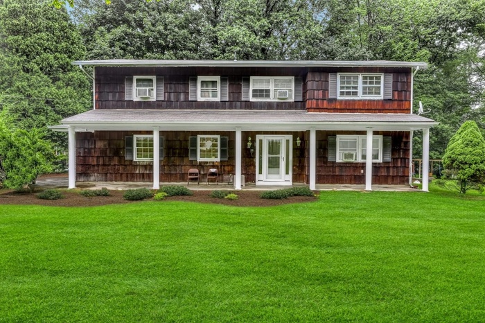 View of front of property featuring a porch, a front lawn, and view of wooded area
