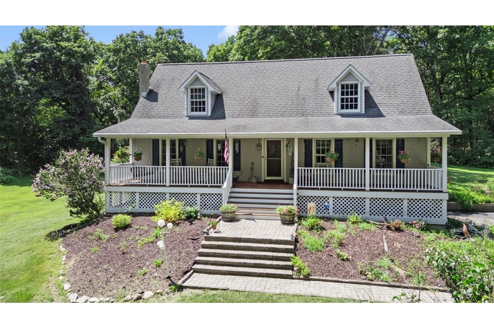 View of front of property with roof with shingles, covered porch, a chimney, and view of wooded area
