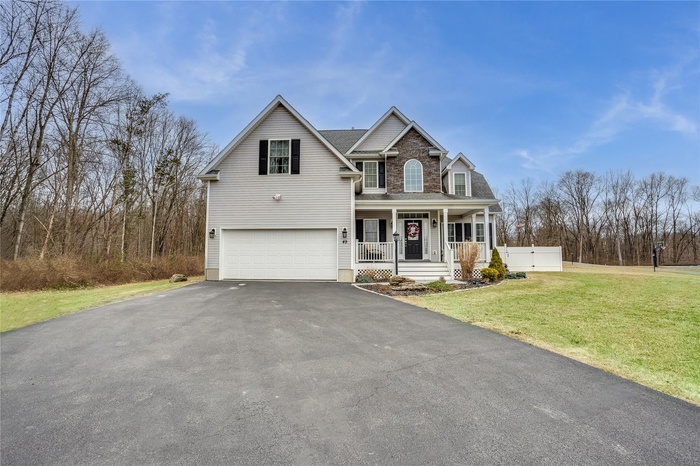 View of front of home featuring an attached garage, covered porch, a shingled roof, driveway, and a front yard