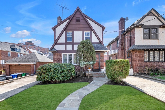 Tudor-style house with a front lawn, brick siding, and roof with shingles