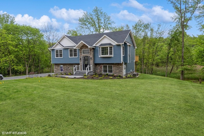 Raised ranch with a front lawn, stone siding, central AC unit, and driveway. Yard is virtually enhanced.