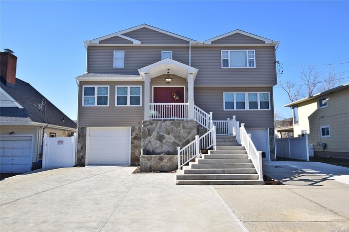 View of front of property featuring driveway, an attached garage, stone siding, and stairs