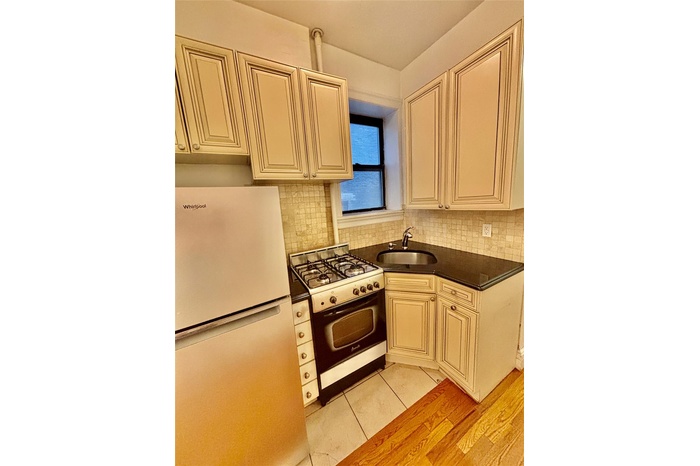 Kitchen with freestanding refrigerator, range with gas cooktop, dark countertops, cream cabinetry, and tasteful backsplash