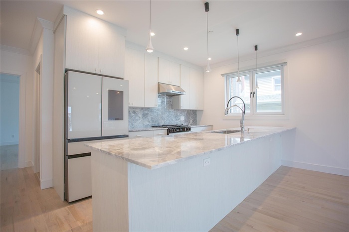 Kitchen featuring freestanding refrigerator, light wood-type flooring, white cabinets, decorative backsplash, and a peninsula