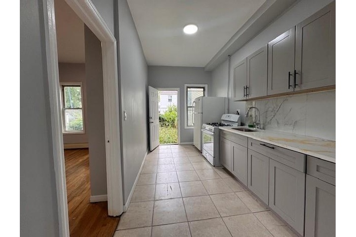 Kitchen with white range with gas stovetop, gray cabinets, light countertops, backsplash, and light tile patterned floors