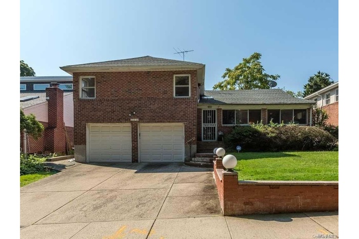 Tri-level home featuring brick siding, driveway, an attached garage, and a front yard