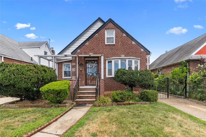 Cape Cod-style house with brick siding, a front yard, porch and a gate