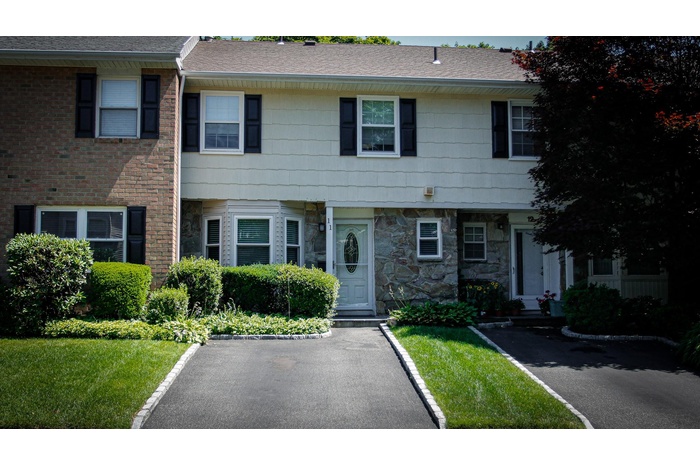 Townhome / multi-family property featuring stone siding, a shingled roof, and a front lawn