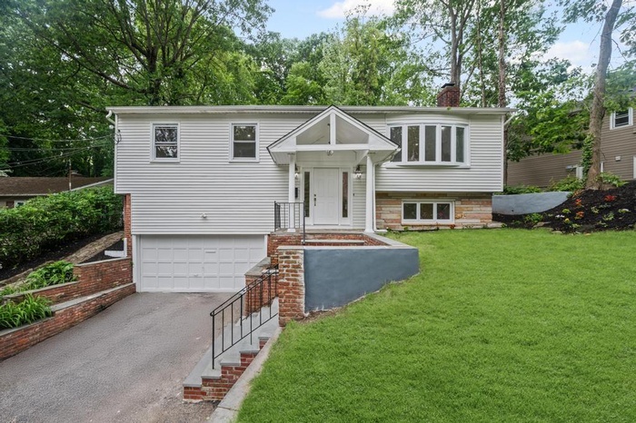 Raised ranch featuring driveway, a chimney, a garage, and a front lawn