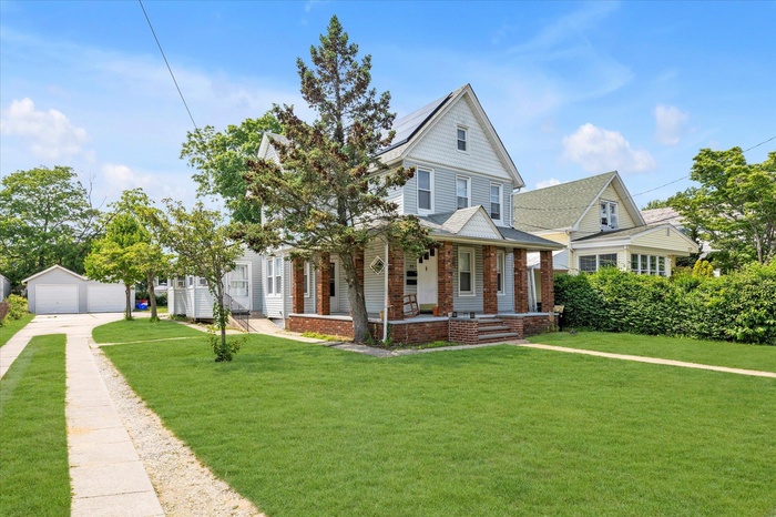 View of front of house with a garage, covered porch, a front lawn, and an outdoor structure
