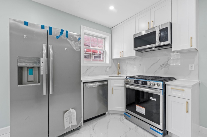 Kitchen with stainless steel appliances, white cabinets, light countertops, light marble finish floors, and tasteful backsplash
