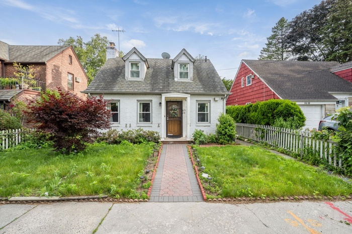 Cape cod-style house featuring a chimney and brick siding