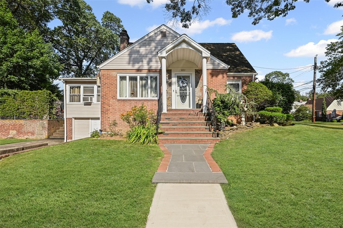 View of front of house with brick siding, a front yard, and a chimney