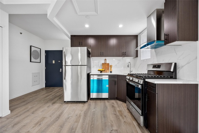 Kitchen featuring stainless steel appliances, wall chimney exhaust hood, dark brown cabinets, light countertops, and recessed lighting