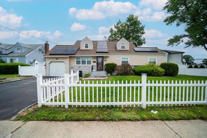View of front facade featuring an attached garage, asphalt driveway, roof mounted solar panels, and stone siding