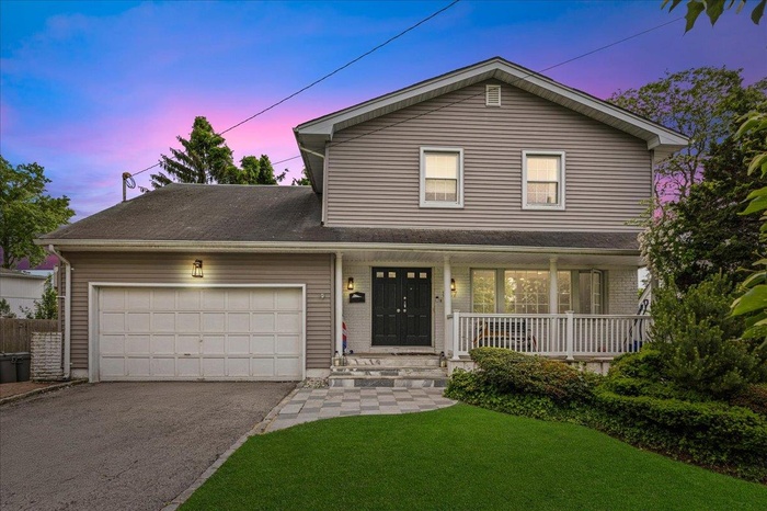 Traditional home featuring an attached garage, driveway, a porch, and a lawn