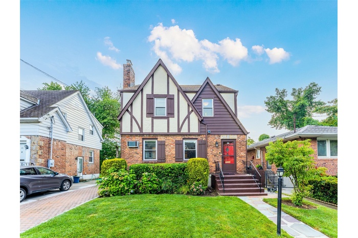 English style home with a chimney, brick siding, and a front lawn
