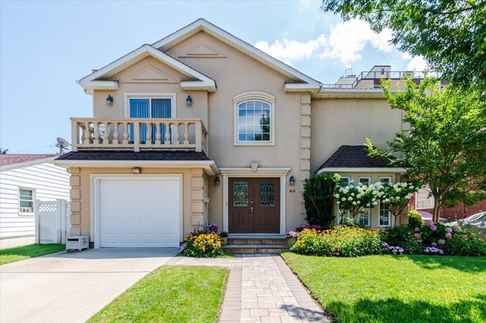 View of front facade with stucco siding, concrete driveway, an attached garage, a front yard, and a balcony