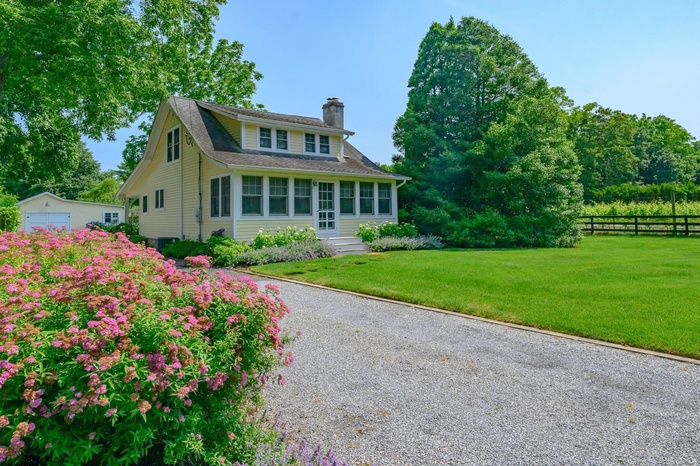 View of front of home featuring a chimney, a detached garage, an outbuilding, roof with shingles, and gravel driveway