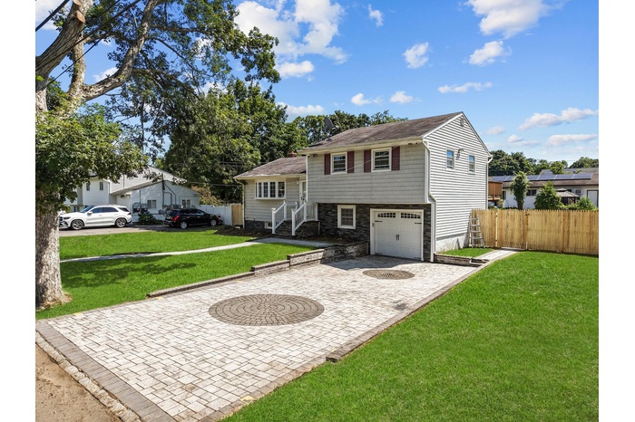 Split level home with an attached garage, decorative driveway, and stone siding
