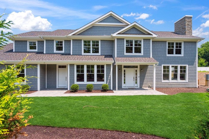 Shingle-style home with a chimney, a shingled roof, and a front lawn