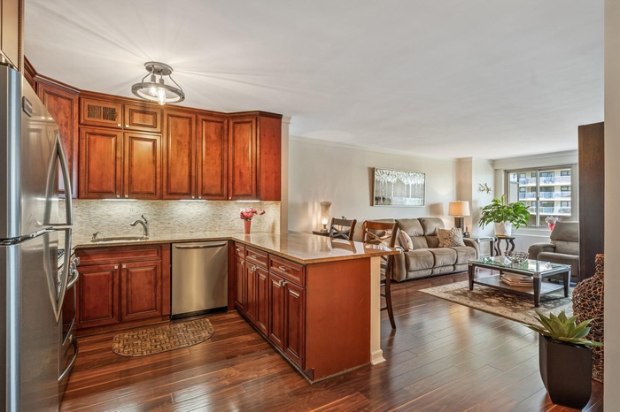 Kitchen with stainless steel appliances, a peninsula, dark wood-style flooring, tasteful backsplash, and light stone Granite counters
