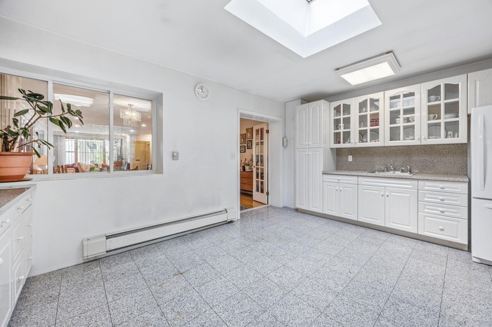 Kitchen featuring baseboard heating, granite floors, glass insert cabinets, and white cabinetry