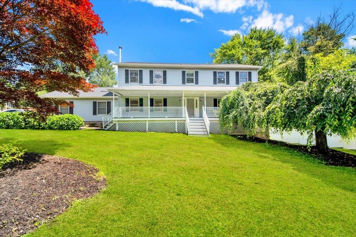 Colonial home with covered porch with recessed lighting, stairs, and a front lawn. Front bed blooms with spring bulbs and hydrangeas bloom all summer!