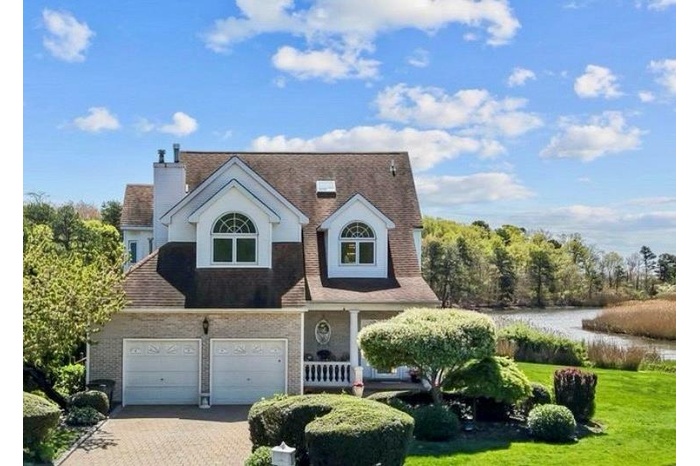 View of front of property featuring brick siding, driveway, a front yard, a water view, and a porch