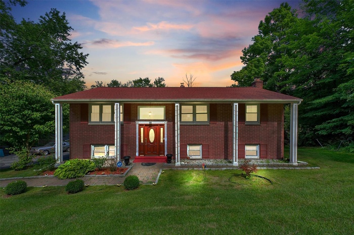 Bi-level home featuring a lawn, a chimney, brick siding, and a porch