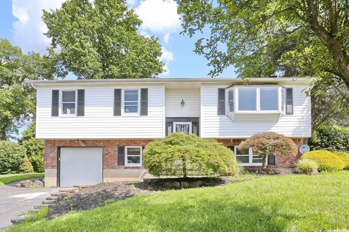Raised ranch with brick siding, an attached garage, driveway, and a front lawn
