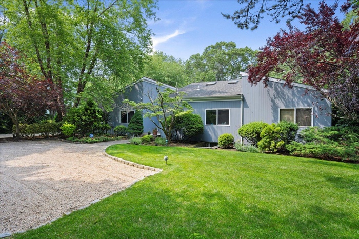 Back of house featuring a lawn, dirt driveway, and roof with shingles