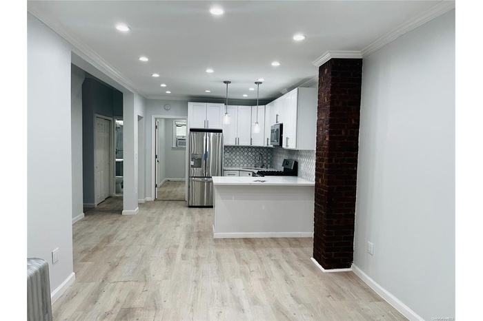 Kitchen with stainless steel appliances, crown molding, decorative backsplash, white cabinetry, and light countertops