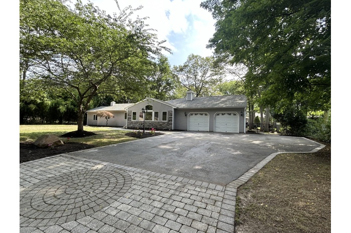 View of front of home with asphalt driveway, a garage, a chimney, stone siding, and a front yard