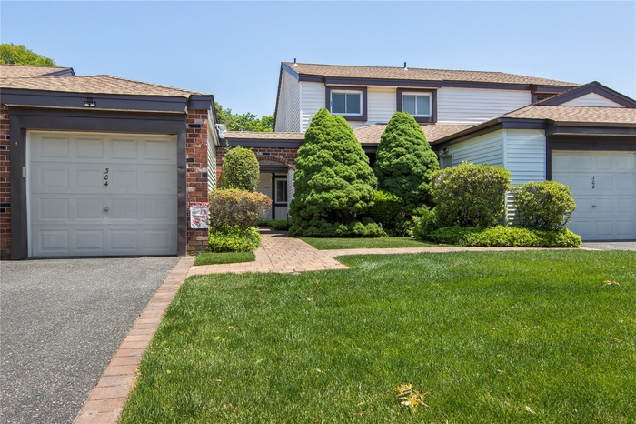 Traditional home with a front yard, brick siding, roof with shingles, driveway, and a garage