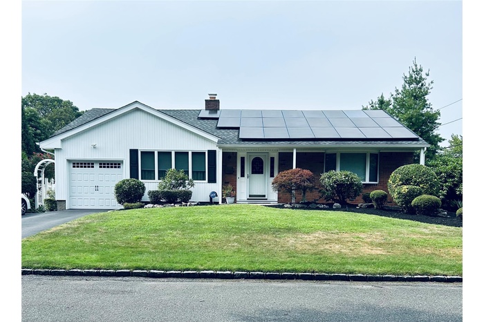 View of front of property with a garage, a front lawn, roof mounted solar panels, a chimney, and driveway