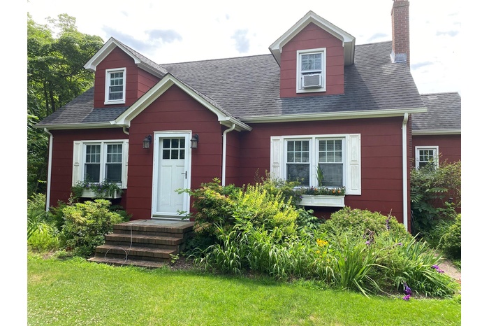 New england style home with a chimney, a shingled roof, and a front yard