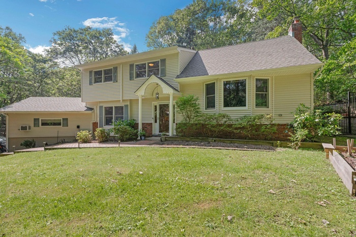 Tri-level home featuring a front lawn, a chimney, a shingled roof, and brick siding