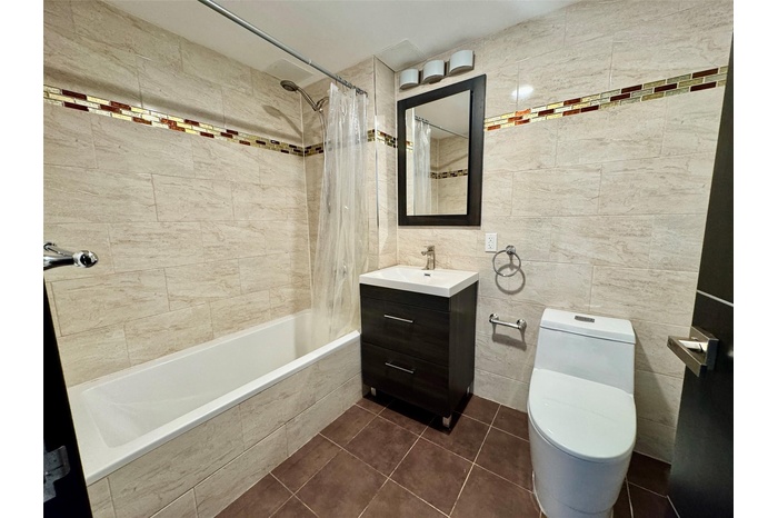 Full bathroom with tile walls, vanity, toilet, tile patterned floors, and shower / bath combo with shower curtain