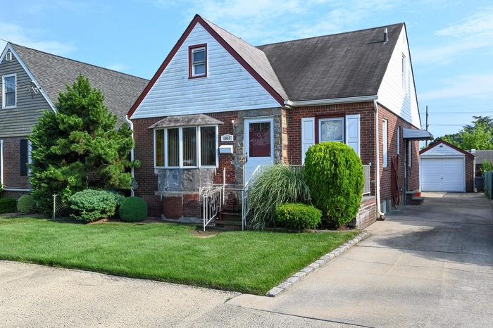 View of front of property featuring brick siding, an outdoor structure, concrete driveway, a front lawn, and a detached garage