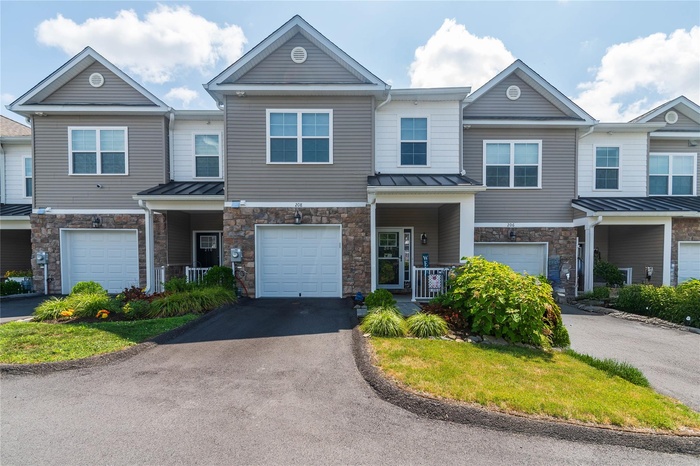 Townhome property featuring stone siding, an attached garage, and driveway