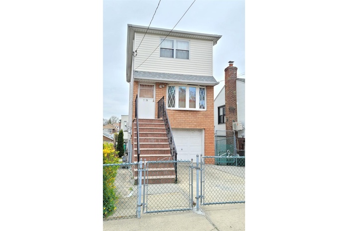 View of front of property featuring a garage, brick siding, driveway, and a fenced front yard